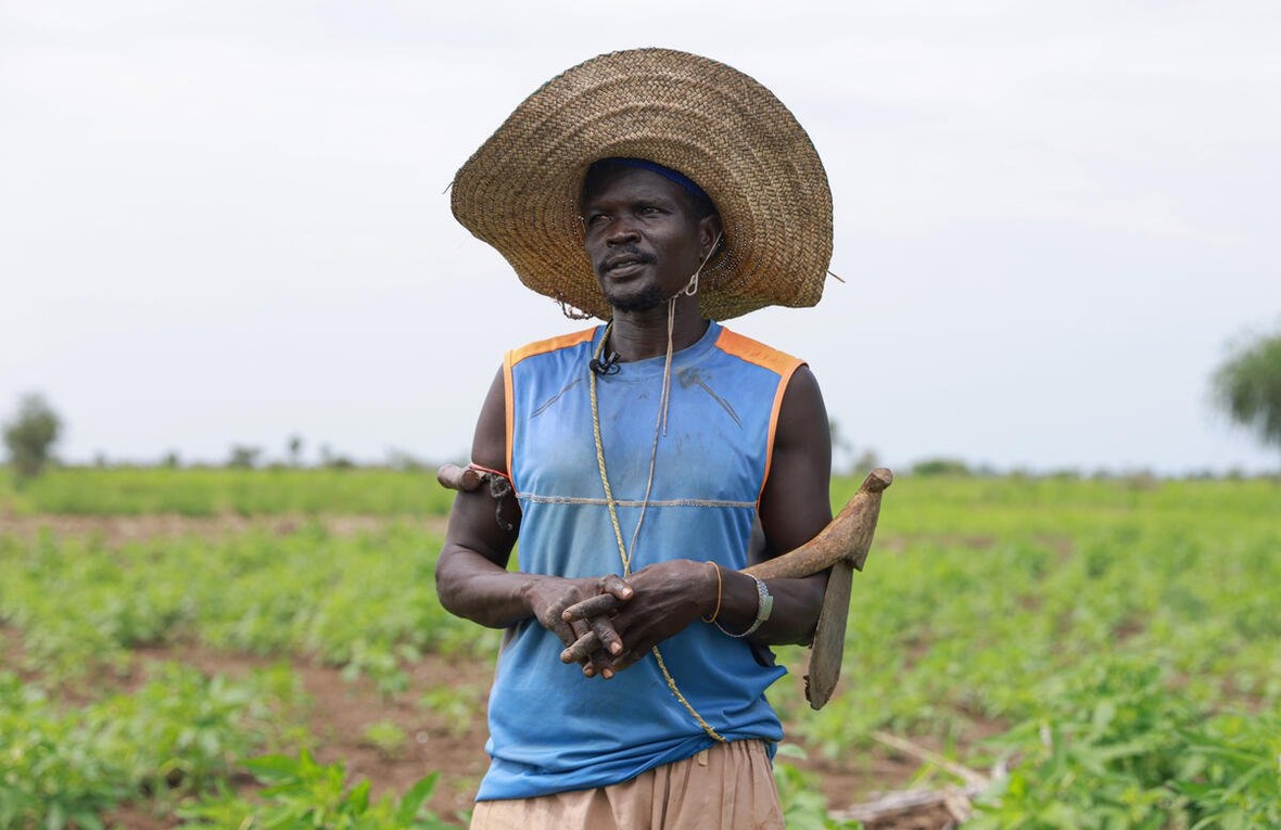  A man wearing a large, straw hat stands in a field.