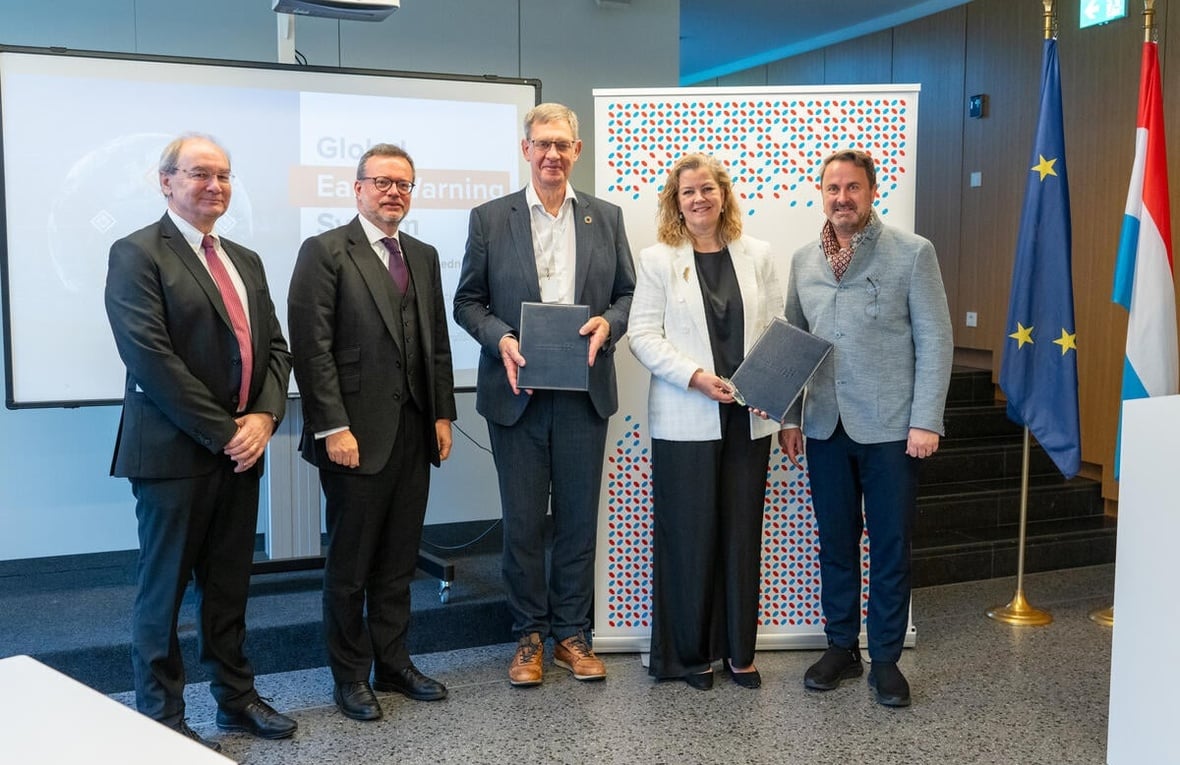 Four men and one woman stand looking at the camera while holding up two documents