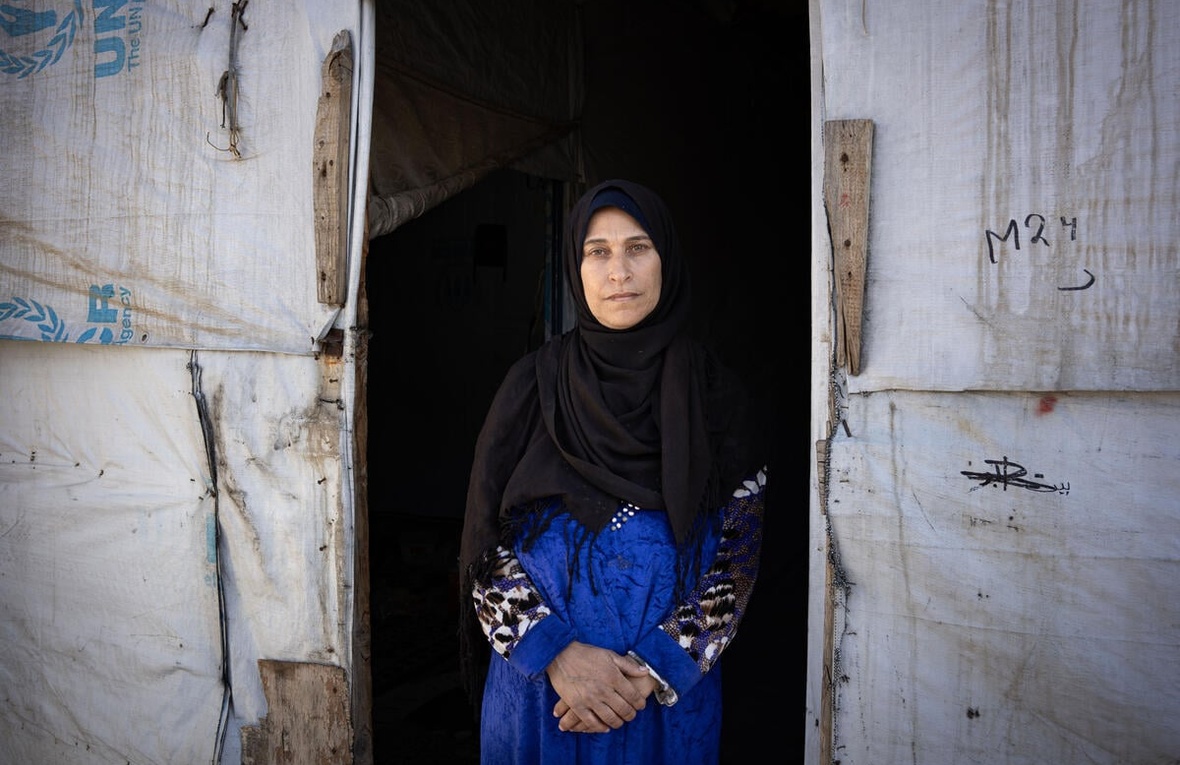 A woman wearing a headscarf stands at the entrance to a UNHCR-branded shelter.