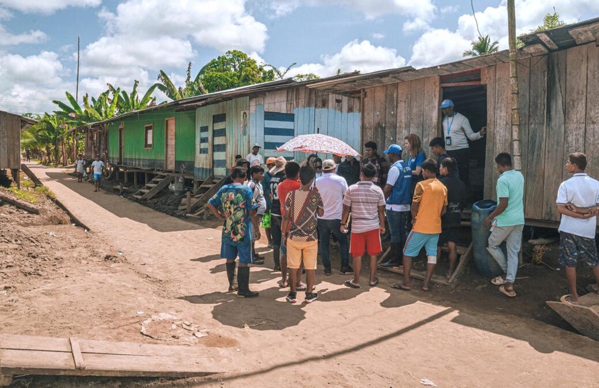 UNHCR staff among a group of people gathered outside a wooden shelter in a row of similar structures.