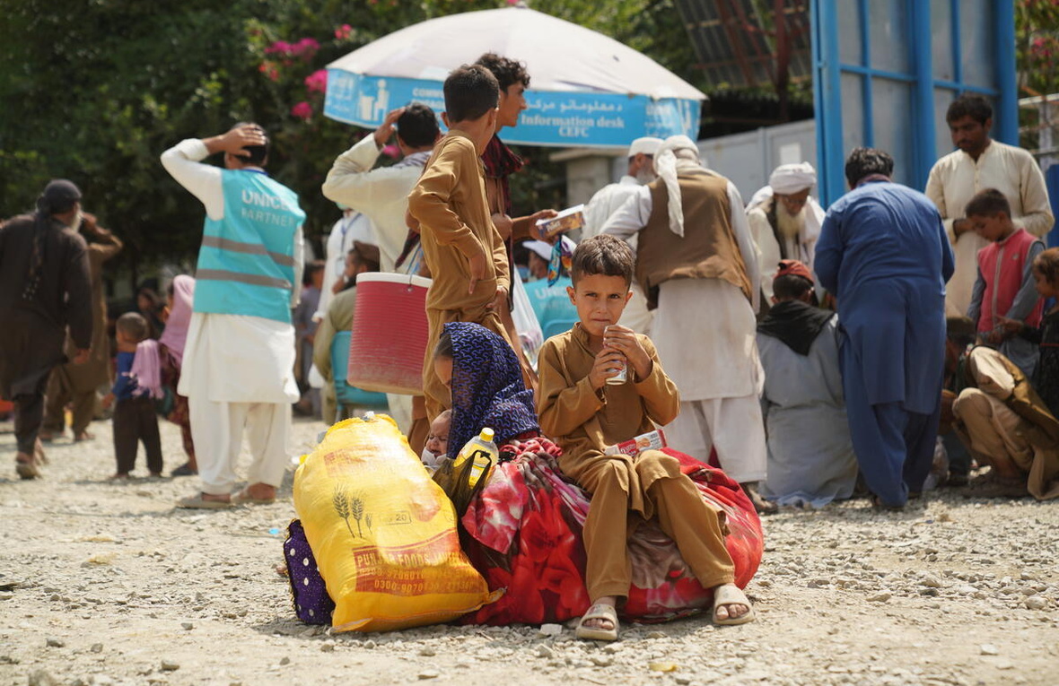 A young Afghan boy sits on piles of luggage, while others stand behind.