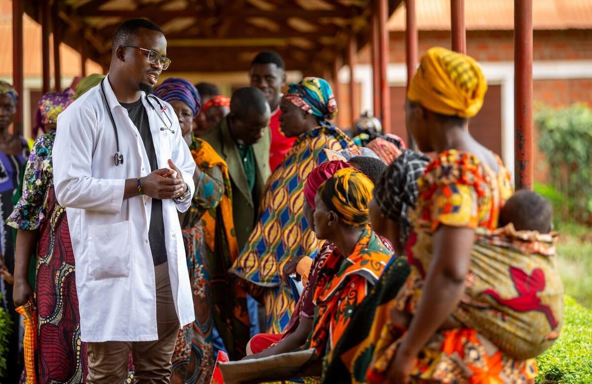 A clinician in a lab coat meets with a group of people outside.