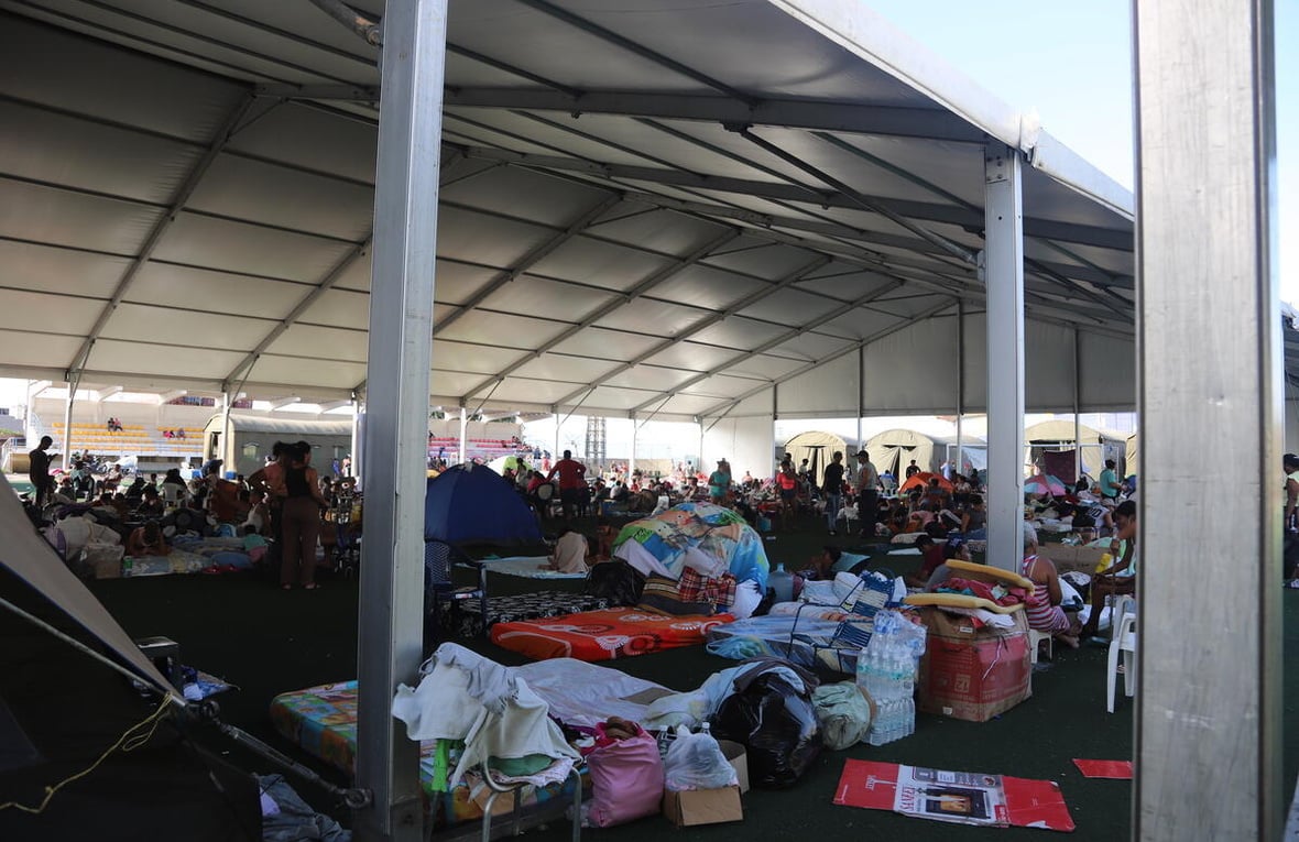 A temporary shelter filled with supplies and people in the background