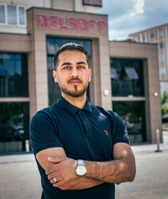 A man with folded arms looks at the camera. He's standing outside, a BELSOFT building behind him.