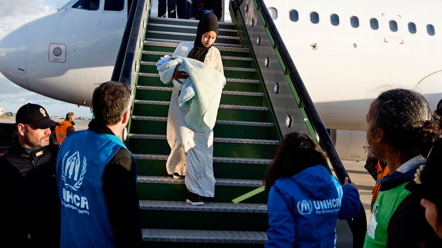 A Somali woman holding a baby is greeted by UNHCR staff as she exits a plane after being evacuated from Libya to Italy. 