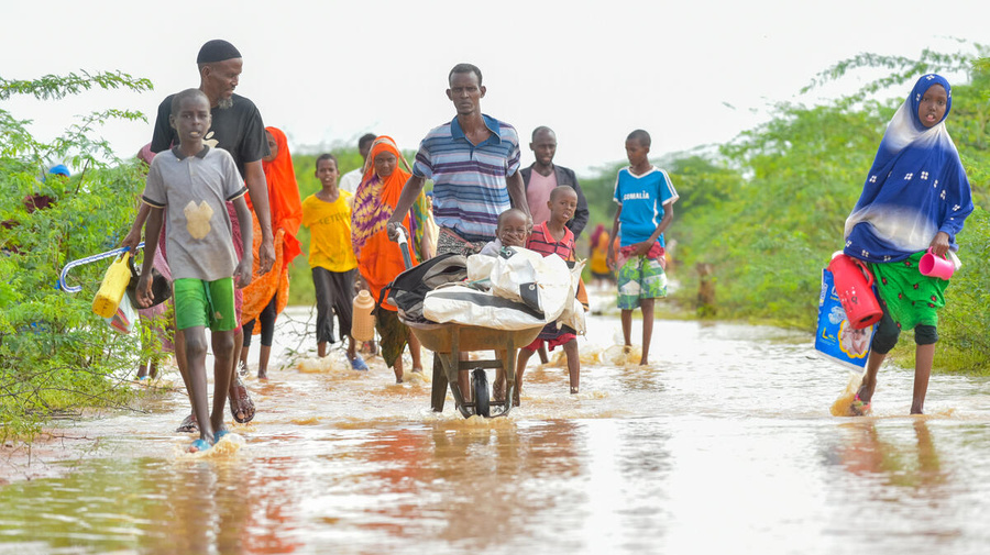 A man pushes a handcart containing a young child and his belongings through floodwaters accompanied by other family members.