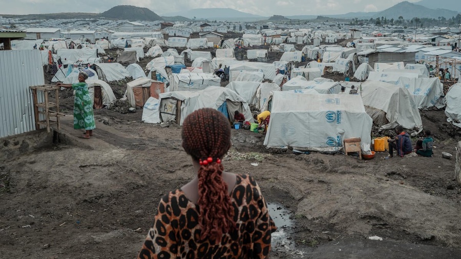 A rear view of a woman standing on muddy ground in front of hundreds of tents stretching to the horizon.