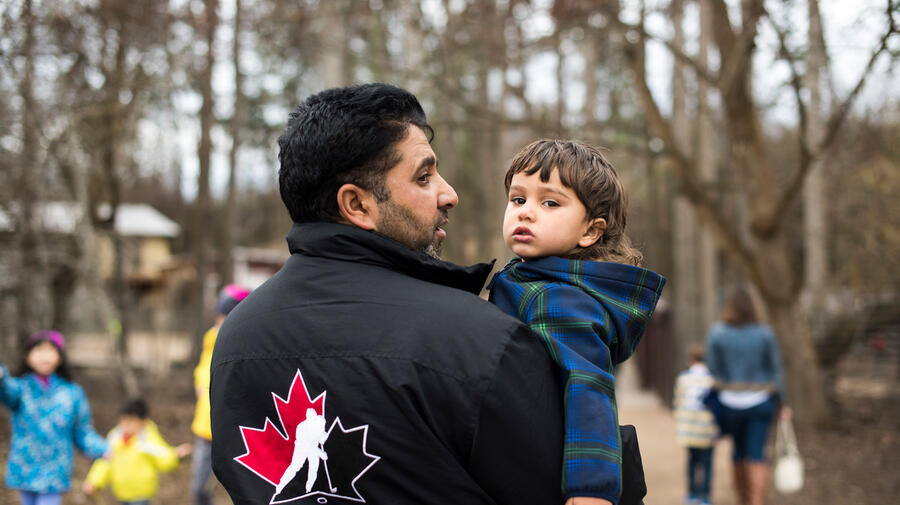 Canada. Mohammad, a Syrian refugee man carrying his youngest son at a petting zoo