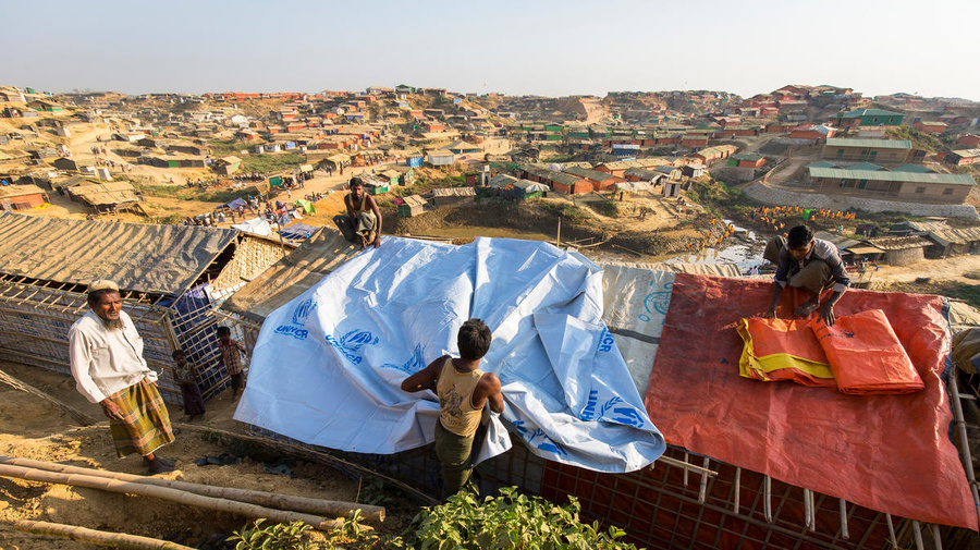 Four men spread tarpaulin's on a roof of a shelter.