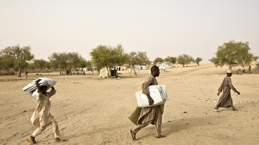 Nigerian refugees carry plastic sheeting to cover shelters at Sayam Forage refugee camp in Diffa, Niger.