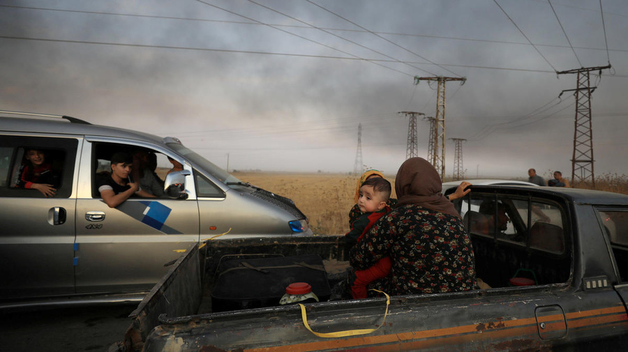 Syria. A woman with a baby sits at a back of a truck as they flee Ras al Ain town