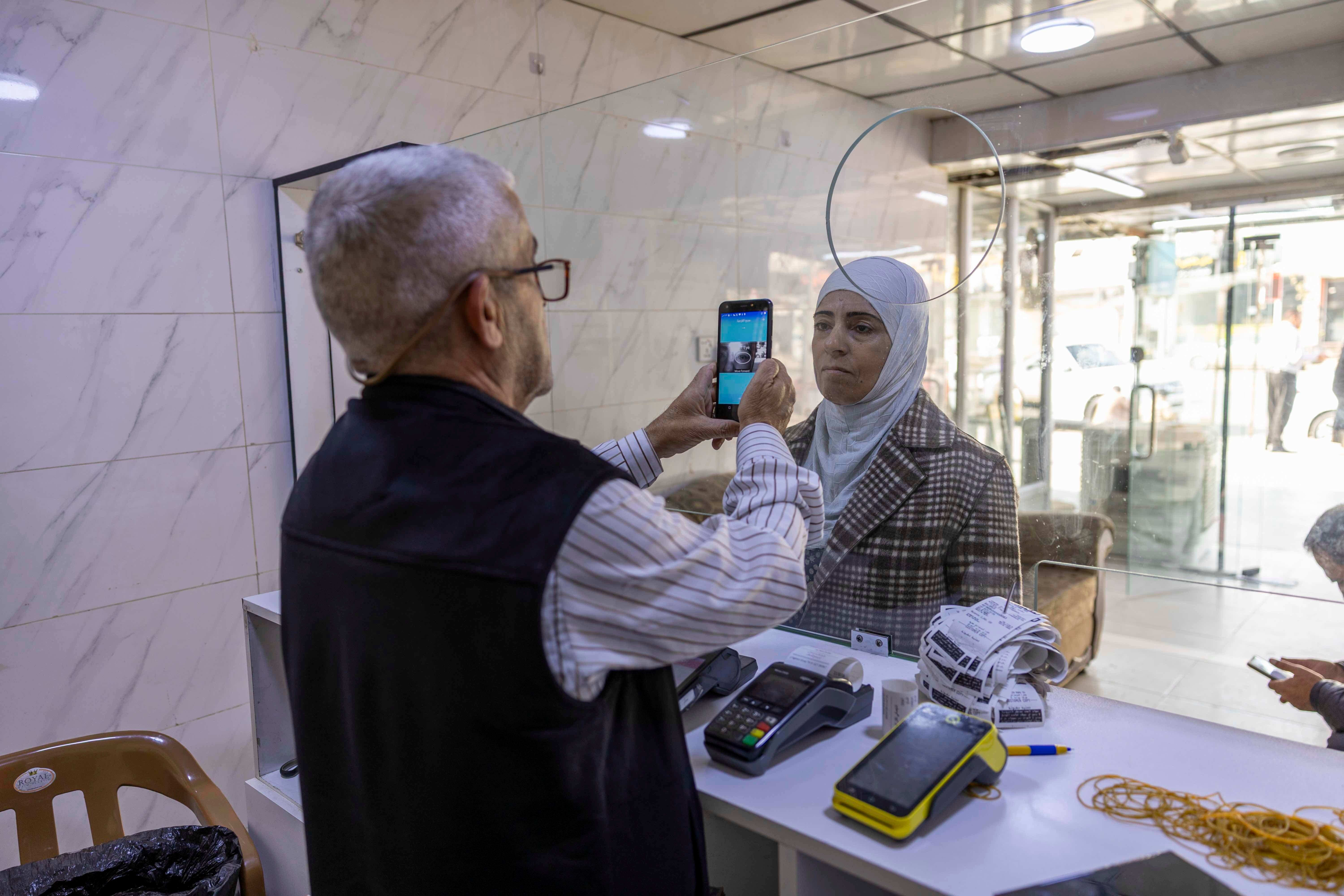 The cash agency scans Eiman's eye with an IRIS scanner to confirm her identity before she receives her aid.