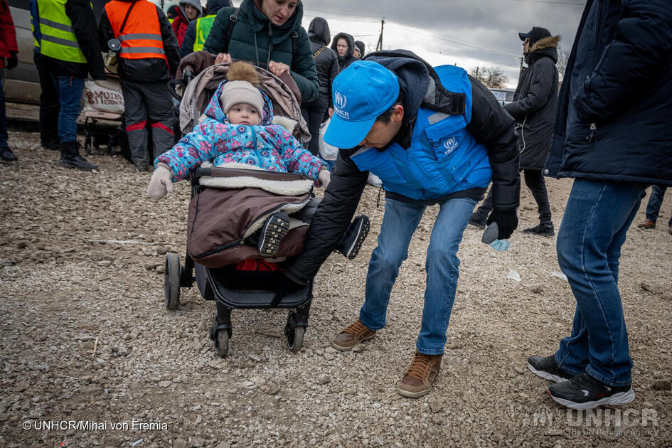 Il responsabile della protezione dell'UNHCR Batyr Sapbyiev aiuta una madre e suo figlio a raggiungere gli autobus in attesa al valico di frontiera di Palanca, in Moldavia. © UNHCR/Mihai Eremia