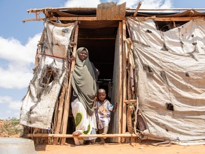 A woman and her young child stand in the entrance of a makeshift shelter.