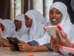 Girls in a white hijab sitting in a classroom holding tablets