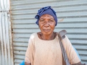Older woman in blue headscarf standing outside her house
