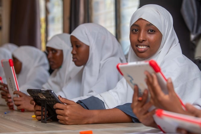 Girls in a white hijab sitting in a classroom holding tablets
