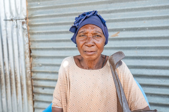 Older woman in blue headscarf standing outside her house