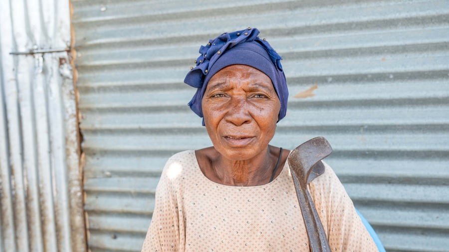 Older woman in blue headscarf standing outside her house