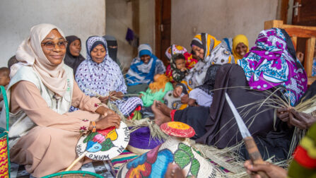 A group of women sit on the floor weaving colourful baskets.