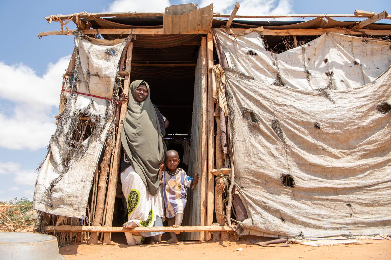 A woman and her young child stand in the entrance of a makeshift shelter.