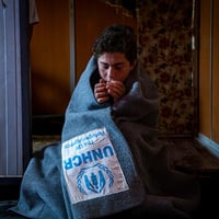 Jordan. Omran, 12 years old Syrian refugee, warming himself using UNHCR blanket inside their shelter in Zaatari refugee camp.