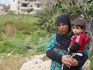 A Syrian woman holds her young nephew in a field near their home