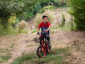 A young boy in a red t-shirt sits on his bike.
