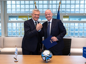 Two men shake hands behind a desk with a football on it.