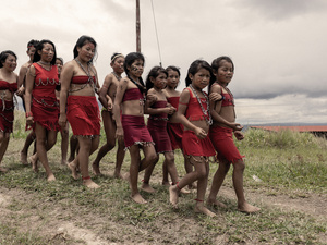A group of young indigenous people wearing traditional dress walk together near their village