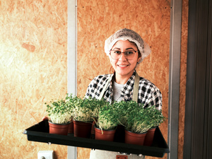 Une femme coiffée d'un filet à cheveux transporte un plateau de micropousses.
