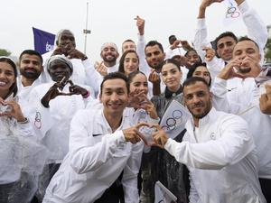 A group of young men and women wearing white tracksuits make heart emojis with their fingers.