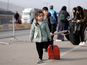 A young child walks on asphalt pulling a small suitcase.