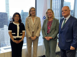 Four people stand looking at the camera inside an office building, a view of New York city behind them through the window.