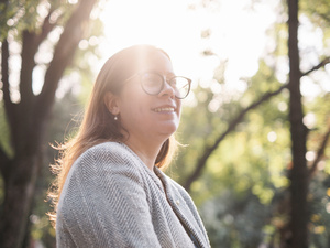 Sunlight shines through trees onto a woman wearing glasses and a business jacket 