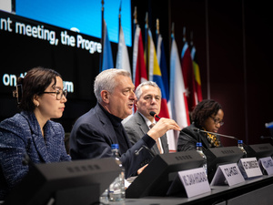 Four persons sitting on stage, one of them speaking into a microphone