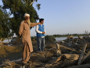 An Afghan man gestures to a UNHCR worker, showing devastation caused by a monsoon.