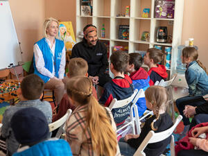 Mexican actor Alfonso Herrera and a UNHCR staff member sit in a classroom in front of rows of children. 