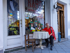 A smiling woman seated at a table in front of a café with colorful paintings on the windows and doors.