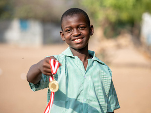 Un jeune Somalien de 14 ans pose à l'extérieur, souriant et tenant une médaille.