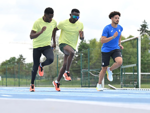 Trois athlètes courent en parallèle sur une piste de course bleue.