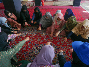 A group of women seated in a circle on a rug put their fists together.