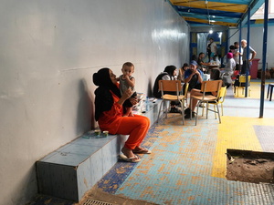 A woman sits on a ledge in a courtyard with a small boy standing on her lap.