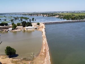Flooding surrounds buildings, trees and a long bridge.