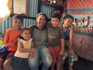 A mother sits on a bed in a shack with her four children.