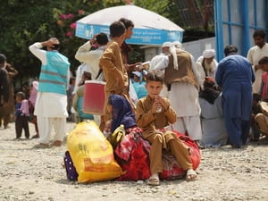 A young Afghan boy sits on piles of luggage, while others stand behind.