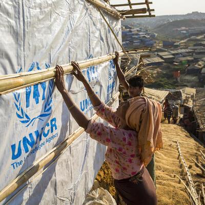 Two refugees build a shelter with bamboo poles and tarpaulins