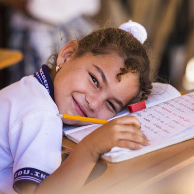 A girl smiles while leaning on her open notebook in a classroom at a school in Colombia.