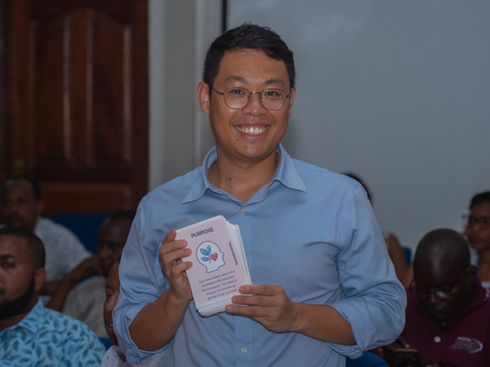 A smiling man holds up a card which reads 'Purpose' during a training session