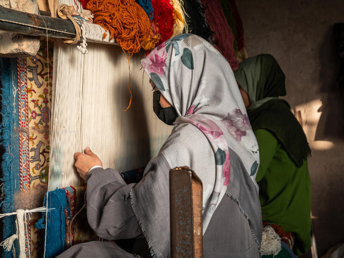 A woman weaving a carpet on a loom.